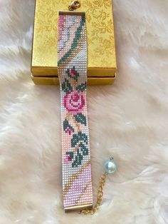 a gold box with a pink and green beaded tie on it next to a chain