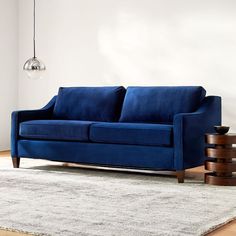 a blue couch sitting on top of a wooden floor next to a table and lamp