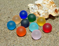 there are many different colored glass balls on the ground next to a seashell with a shell