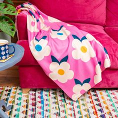 a pink couch with a flowered blanket on it and a coffee cup sitting next to it