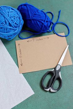 two balls of yarn are next to scissors and a piece of paper on the table