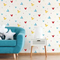 a blue couch with mickey mouse pillows on it in front of a wallpapered background