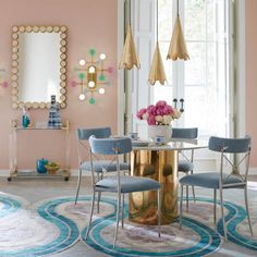 a dining room with pink walls and blue chairs around a round table in front of a mirror