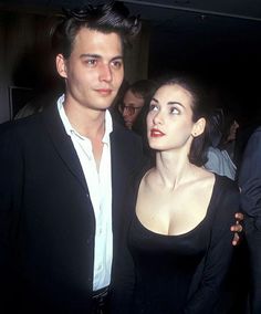 a man standing next to a woman in a black dress at a formal event with other people