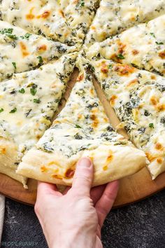 a pizza with cheese and spinach is cut into slices on a wooden platter