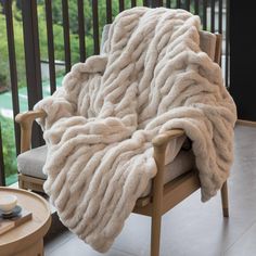 a white blanket sitting on top of a wooden chair next to a cup and saucer