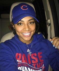 a smiling woman in a blue hoodie and cap sitting in the back of a car