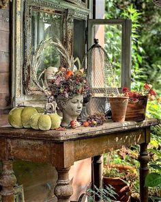 an old wooden table topped with lots of plants and fruit next to a mirror on the wall