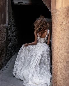 a woman in a white wedding dress is standing by a wall and looking at something