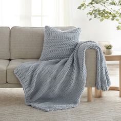 a couch with a blanket on top of it next to a table and potted plant