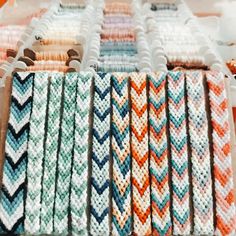 rows of crocheted bracelets on display at a market stall with orange, white and blue colors