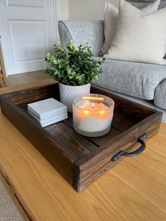 a wooden tray with a candle and some books on it sitting on a table next to a couch