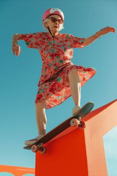 an older woman in a floral dress riding a skateboard on top of a wall