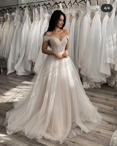 a woman standing in front of a rack of wedding dresses