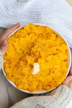 a person holding a bowl of mashed potatoes with butter and seasoning on top