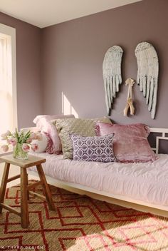 a bed with pink pillows and angel wings on the wall above it in a bedroom