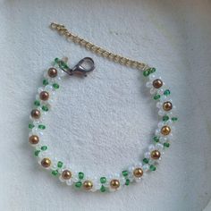 a white and green beaded bracelet on a gold plated chain with a clasp