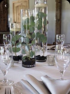 the table is set with silverware and glass vases filled with plants in them