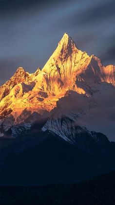 the top of a mountain is lit up at sunset with clouds in the sky above it