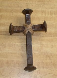 an old rusty metal cross hanging on a wooden wall with a rope attached to it