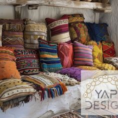 an assortment of colorful pillows and blankets on display in a room with wooden shelves above them