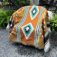 an orange and blue blanket sitting on top of gravel next to potted planters