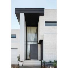 the front entrance to a modern house with white brick walls and black trimmings