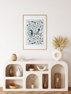 a white shelf with vases and other items on it in front of a wall