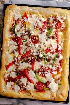 a square pizza with cheese, peppers and other toppings sitting on top of a pan