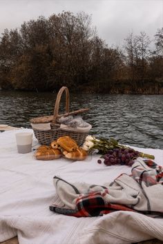 a picnic table with bread, grapes and other food on it next to the water