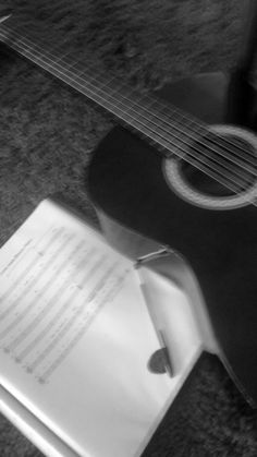 an acoustic guitar laying on the floor next to a piece of paper and pen with writing in it