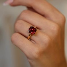 a woman's hand holding a red diamond ring