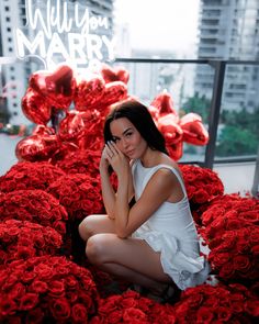 a woman sitting on the ground surrounded by red roses