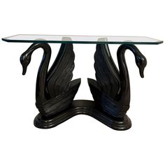 a glass and metal table with two black swans on it's legs, against a white background