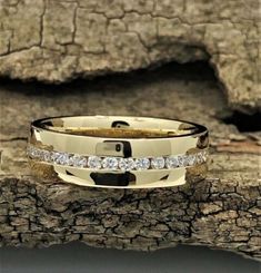 a yellow gold wedding band with white diamonds on top of a tree branch in front of a rock