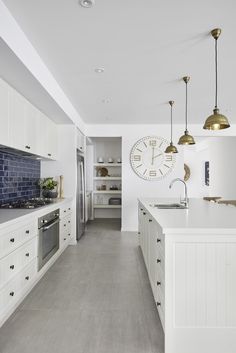 a kitchen with white cabinets and blue tile backsplash, gold pendant lights and a large clock on the wall