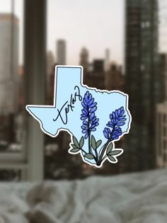 a sticker depicting the state of texas with blue flowers in front of a cityscape