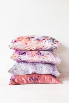 three pillows stacked on top of each other in front of a white wall with paint splatters all over them