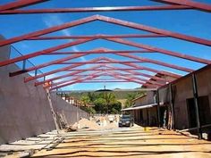 the inside of a building being constructed with red metal beams and wooden slats on the roof