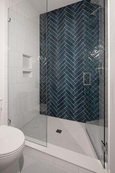 a white toilet sitting next to a walk in shower under a bathroom mirror with blue tiles on the wall