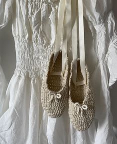 two pairs of crocheted shoes hang on a white dress with laces and bows