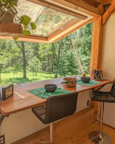 a wooden table sitting under a window next to two bar stools and a potted plant