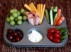 a muffin tin filled with fruit and veggies on top of a table