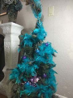 a blue christmas tree with purple and green ornaments on it's top, in front of a white pillar