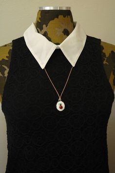 a woman wearing a black dress with a white collar and an apple charm on it