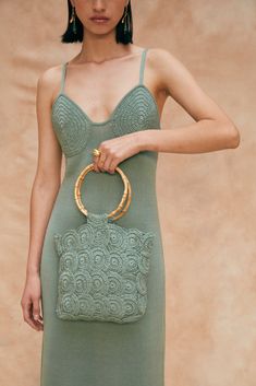 a woman in a green dress holding a handbag with gold accents on the handle