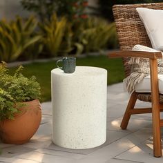 a table with a cup on it next to a chair and potted plant