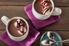 two cups of hot chocolate with marshmallows in them on a purple napkin