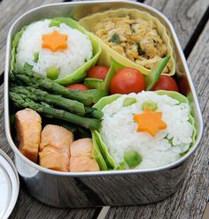 a bento box filled with rice, vegetables and sushi on top of a wooden table