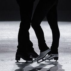 two people in black and white skating on an ice covered rink with their feet touching each other